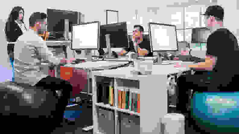 Three people sitting on exercise balls at their desks.