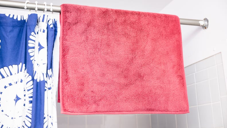 Bath mat drying on a shower rack.