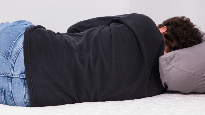 A person sleeping on their side on a mattress.
