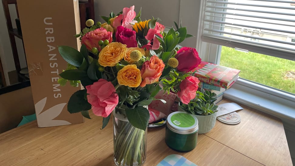 A bright bouquet of flowers from UrbanStems sitting on a wood table by a window