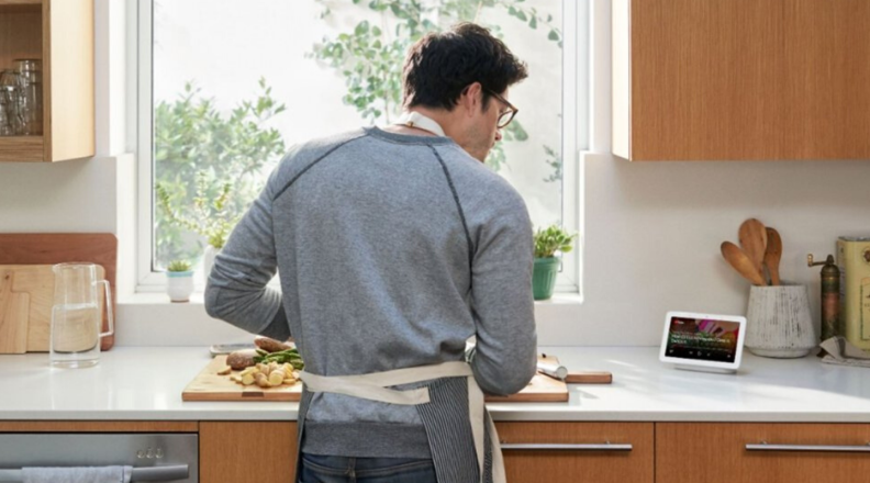 Man standing at kitchen counter following instructions on smart display screen