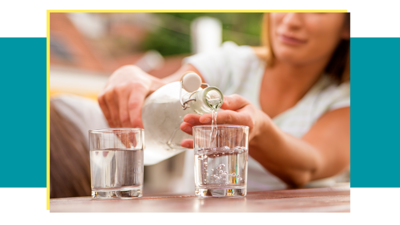 Person pouring water in glass bottle into two glass cups on top of table outdoors.