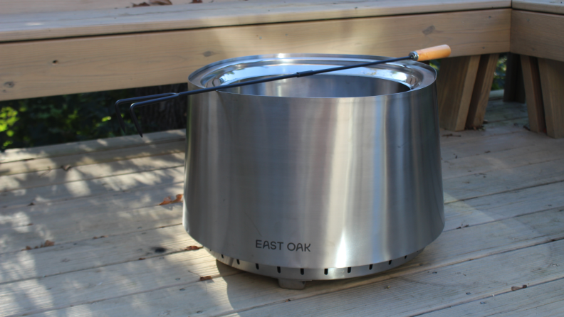 The East Oak Fire Pit sits on a wood deck with the fire poker resting across its opening.