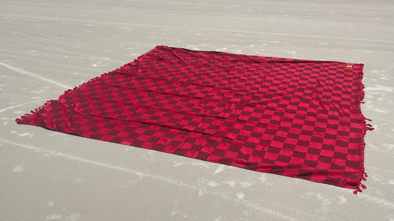 Red and burgundy checkered Big Beachy Blanket on top of sand outdoors.