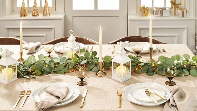 Holiday themed table with candles, green plants, lanterns, plates, and flatware.