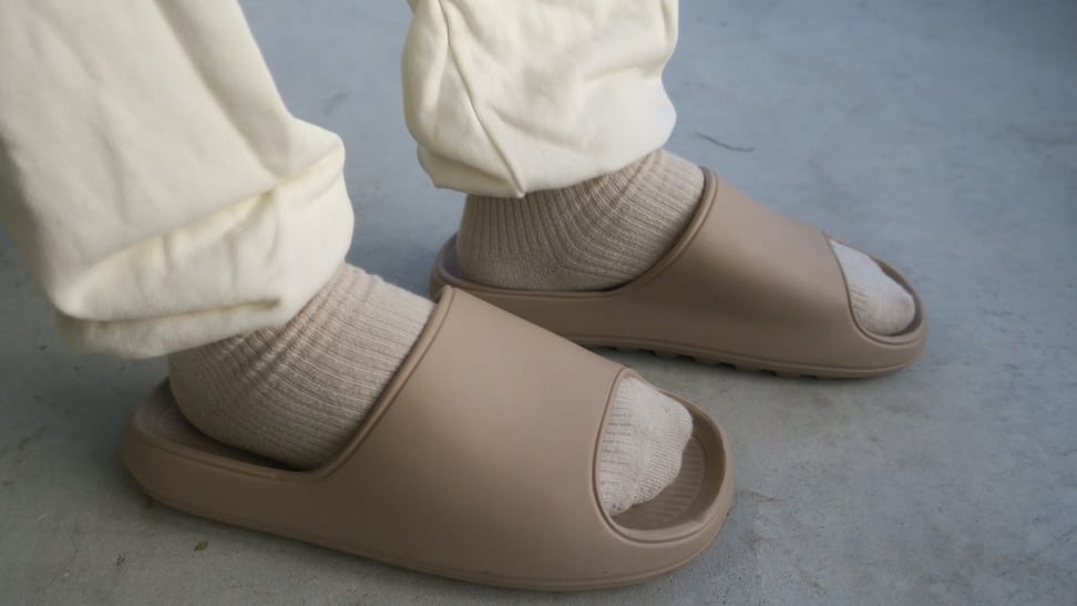 Man's feet in a pair of Litfun slide sandals, which are Yeezy Slide dupes sold on Amazon, in cream colored sweatpants.