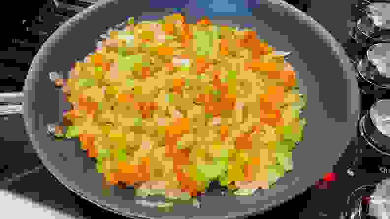 Assorted chopped vegetables cooking in a skillet on top of stove.