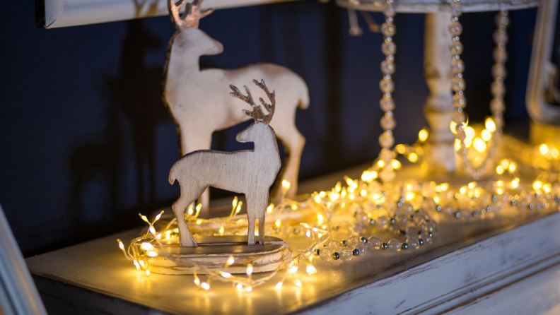 白色壁炉架上挂着一串串LED灯，旁边是木制的驯鹿