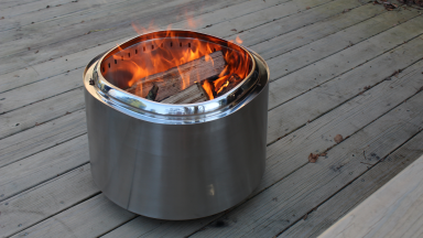 The East Oak fire pit sitting on a wood deck with a large fire burning inside.