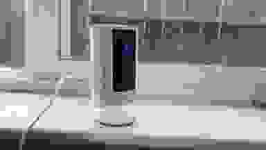 The second-gen Ring Indoor Cam with camera light on sitting on window sill in front of closed window.