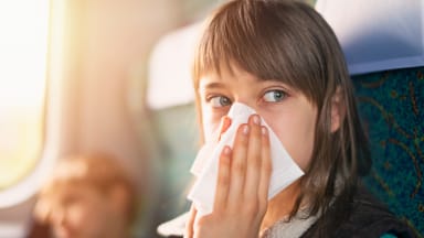 Teenage girl blowing nose on a plane