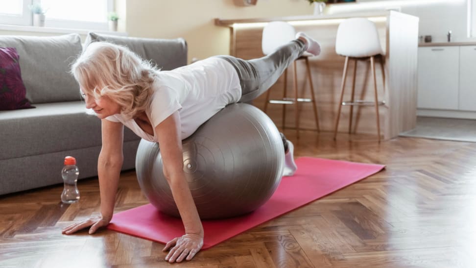 A person balances on a fitness ball in their living room during a workout.