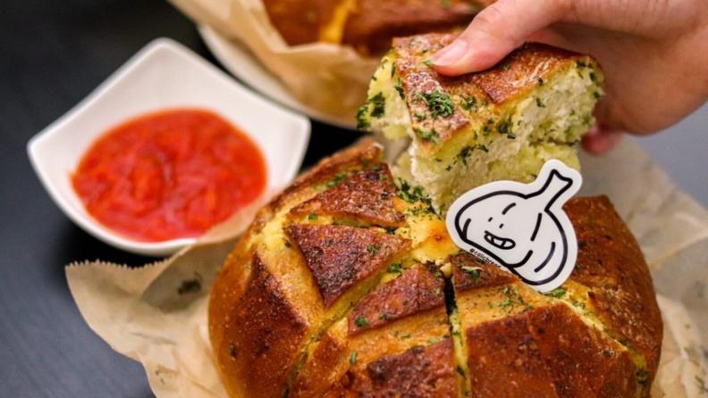 A person is pulling a piece of Korean-style garlic bread by hand. In the back, there's a bowl of dipping sauce.