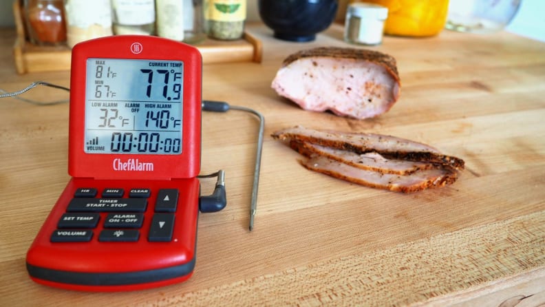 Probe thermometer sits on a wood counter next to sliced meat.