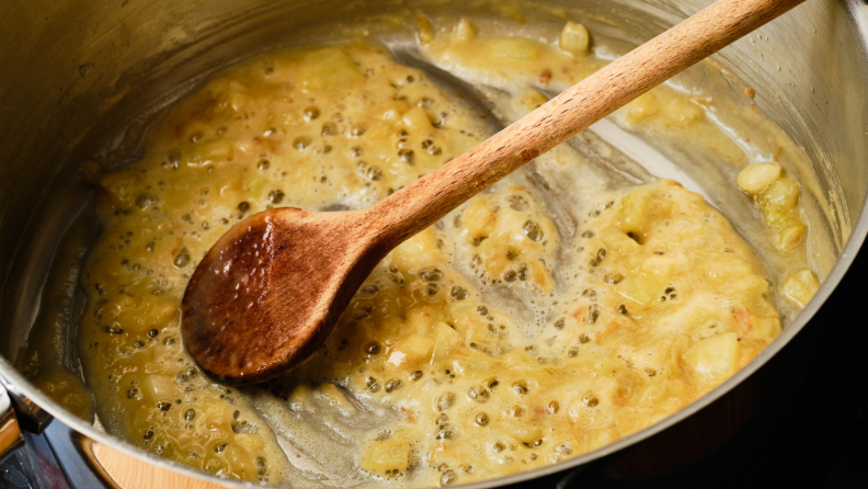 A wooden spoon mixing a roux in a pot.