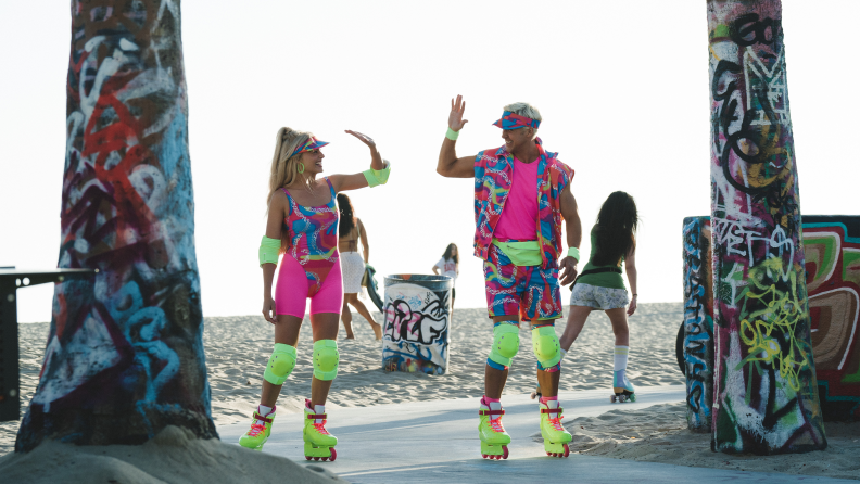 A still from the Barbie movie, where Barbie and Ken are rollerblading on a sidewalk in neon outfits.
