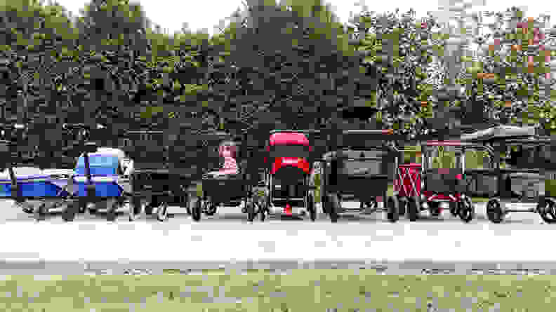 A line of stroller wagons with a young child sitting in one and smiling at the camera.