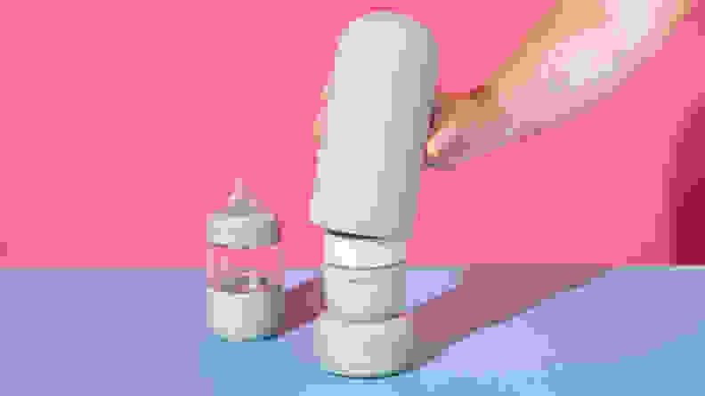 A person grabbing a piece of the Ember Baby Bottle System on a pink and blue background.
