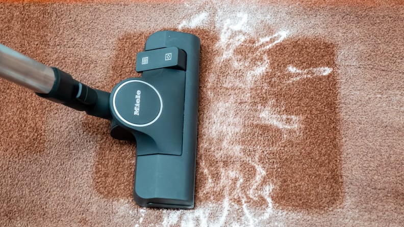 A Miele Boost CX1 vacuum attempts to suck up white powder on a thick brown carpet.