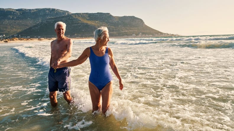 An elderly couple wearing bathing suits walks out of the ocean after a swim