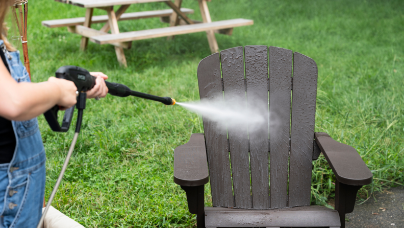 Girl running a pressure washer on an adirondack chair.