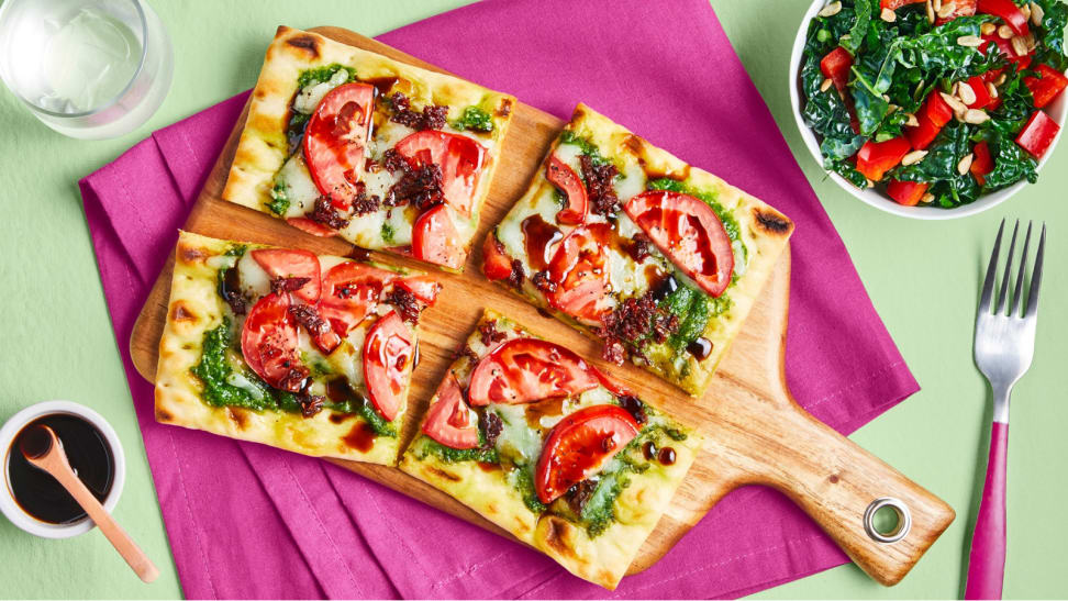 A flatbread pizza on a rectangular cutting board.