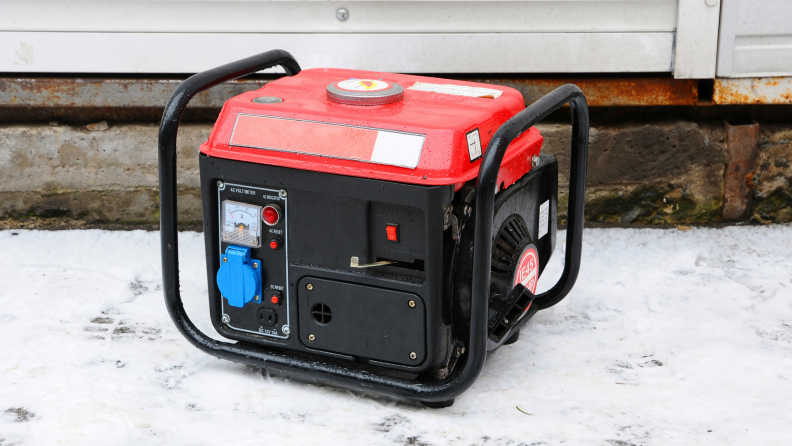 A red portable generator sitting on snow next to house