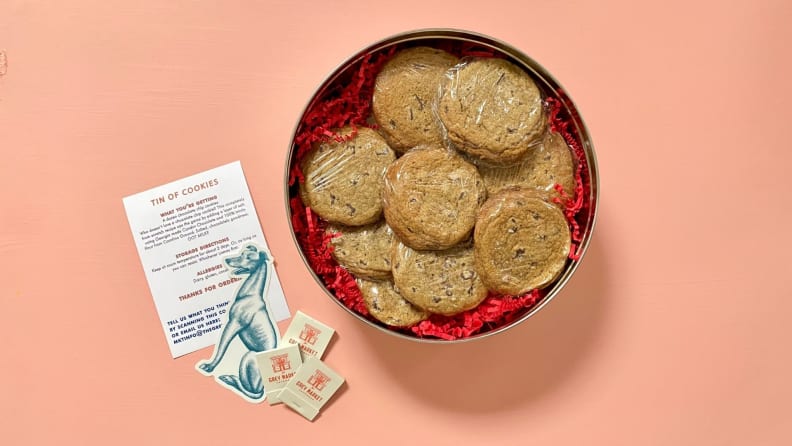 En un tablero rosa hay un frasco de galletas con chispas de chocolate, envueltos individualmente en film transparente, junto con cajas de fósforos y una hoja de información.