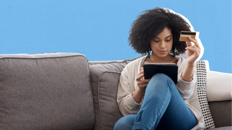 Person sitting on couch while looking at tablet and holding credit card.