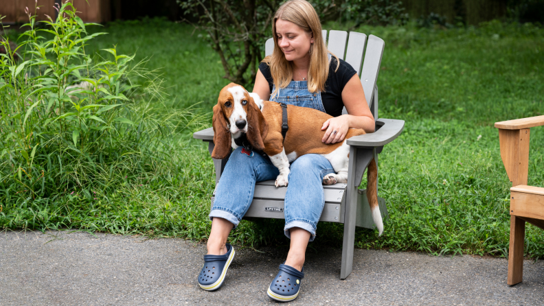 Woman sits with a dog in an adirondack chair.