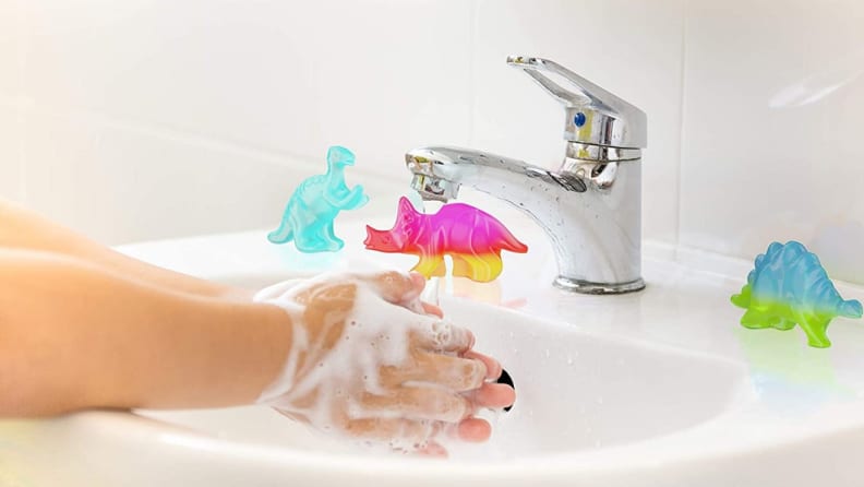 A person washes their hands with dinosaur shaped soap.