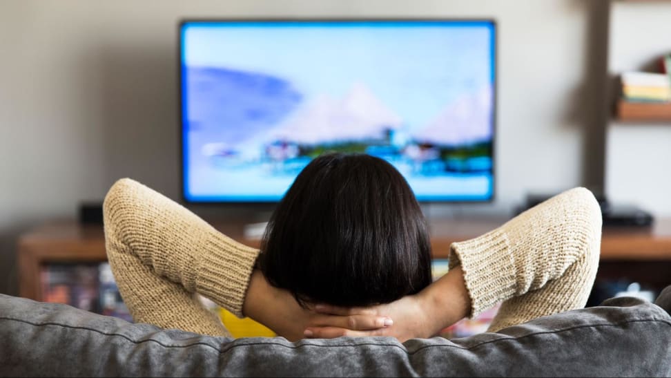 A person lays back on a couch while watching television in a living room.