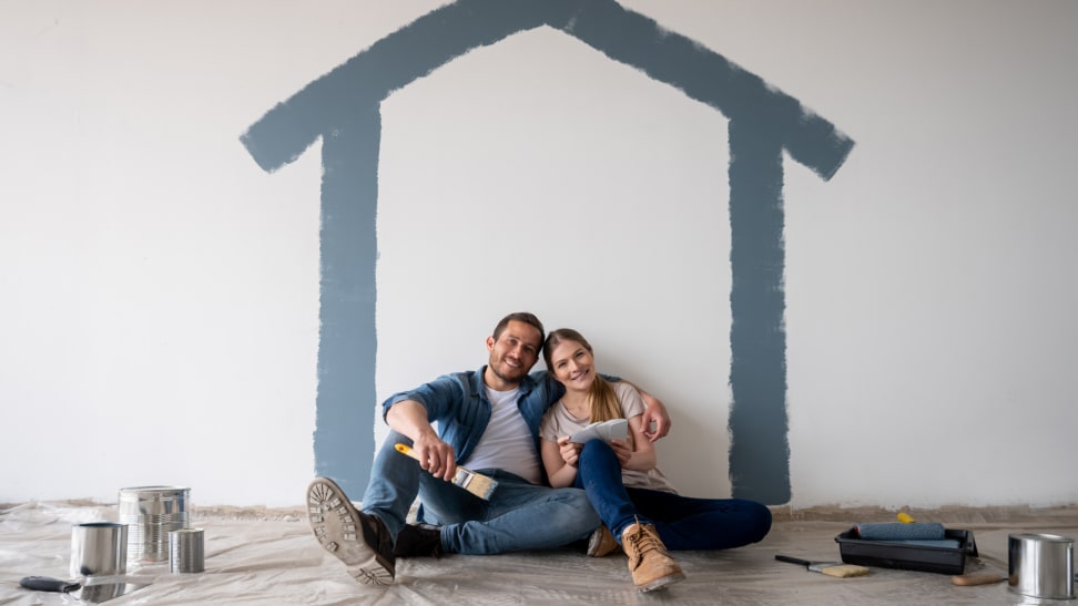 A couple sit inside a room underneath a painted house on a wall.