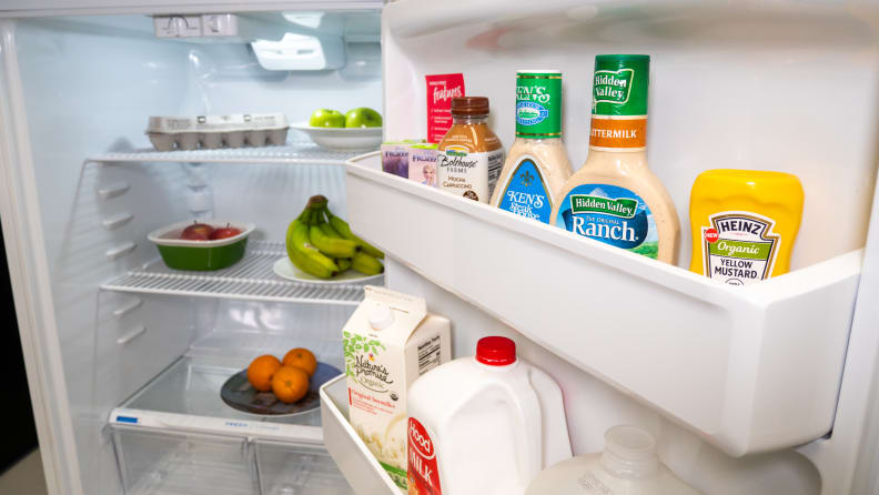 The door and interior of the Frigidaire FFTR1814VW top-freezer refrigerator. The door bins and interior shelves are lined with groceries.