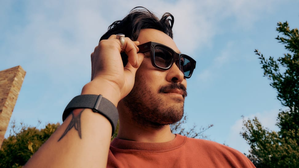 A man wearing Meta Ray-Ban glasses adjusts the frames while looking into the distance outdoors.