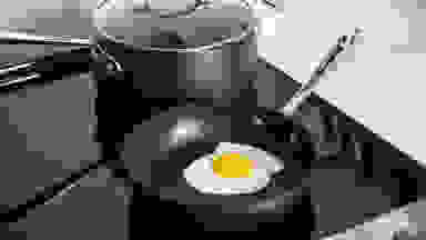 一个完美的煎蛋在不粘锅里，后面有一个不粘锅，都放在炉子上。