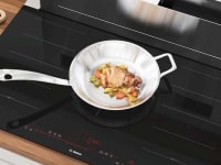 Bosch induction cooktop with chicken cooking on metal pan.