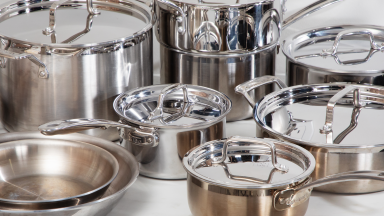 Several stainless steel pots and pans crowded together on a white surface
