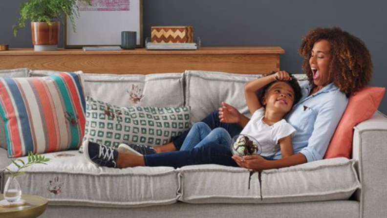 A mother lays with their child on a couch stained with handprints.