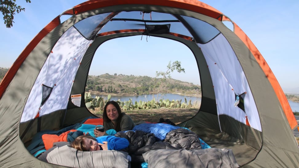 Young child and mother in a camping tent overlooking a lake with cactuses.