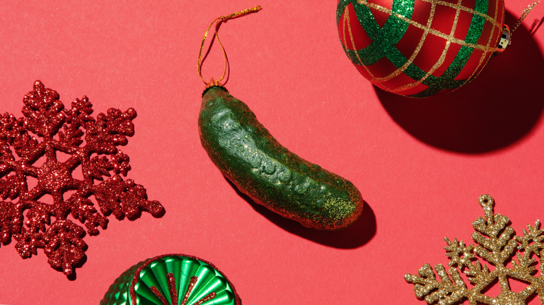 A Christmas pickle ornament on a red background surrounded by ornaments.