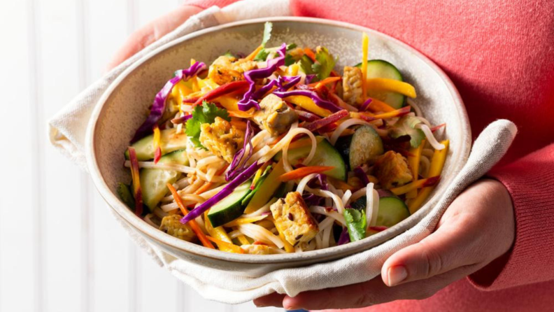 Woman holding noodle bowl.