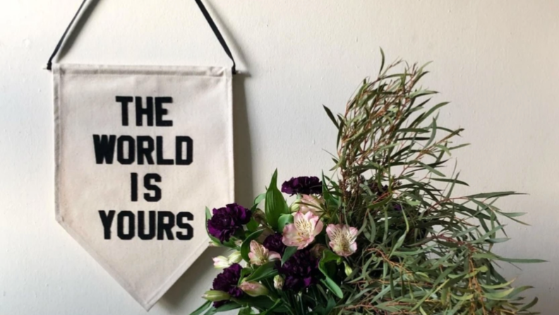 Pennant flag on wall reading 'The World Is Yours' next to flowers in a vase