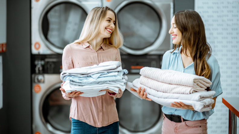 Two people hold stacks of clean towels in a laundromat.
