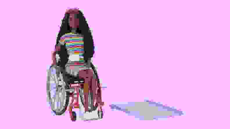 A Barbie in a rainbow-colored dress sits in a wheelchair next to a ramp.