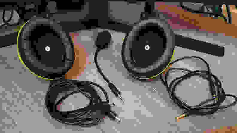 Various pieces and cords from an audio headset are laid out on a desk: a charger, audio cable, mouthpiece, and earphones.