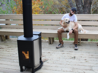 Fire burning inside the Solo Stove Patio Heater with a person and dog sitting on a bench in the background.