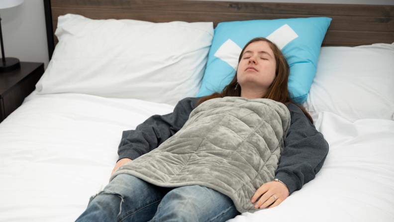 woman laying flat on bed with grey blanket over her torso