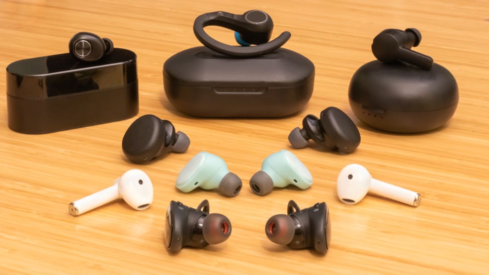Seven pairs of true wireless earbuds laid out on a table surface.