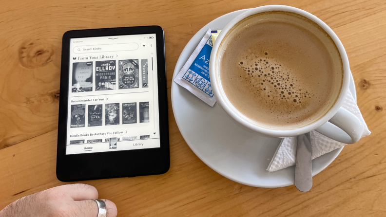 The 11th generation Kindle next to a cup of coffee on a wooden table.